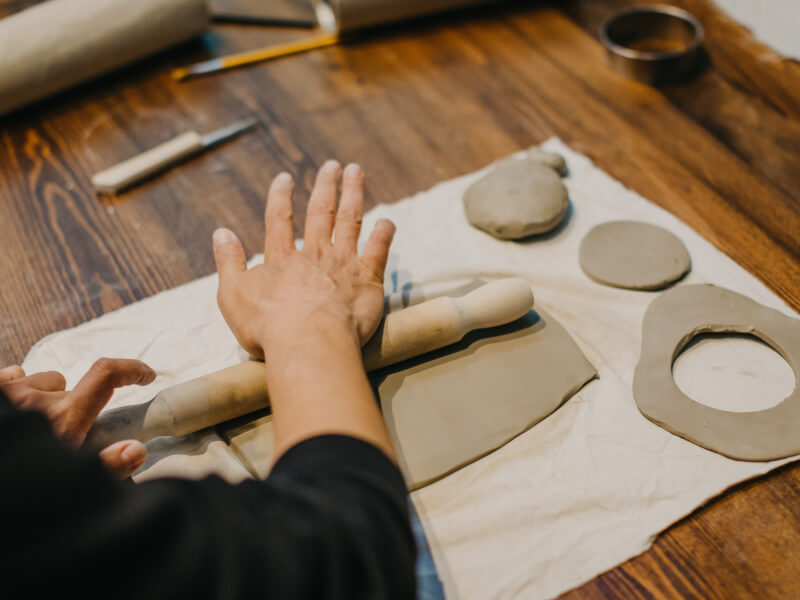 A woman flattening homemade clay using a rolling pin